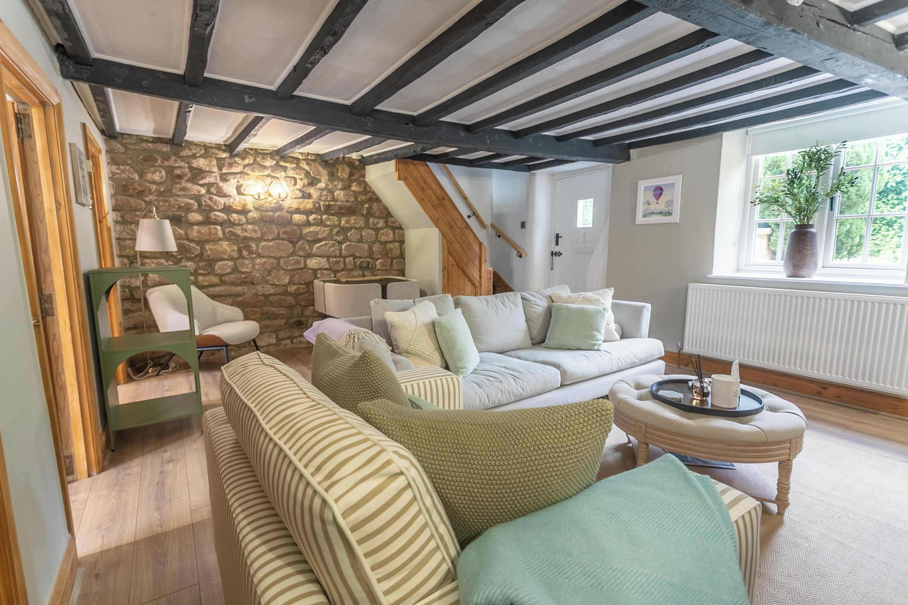 Una sala de estar acogedora con pared de piedra, vigas de madera, un sofá verde, un sofá blanco y una pequeña mesa redonda.