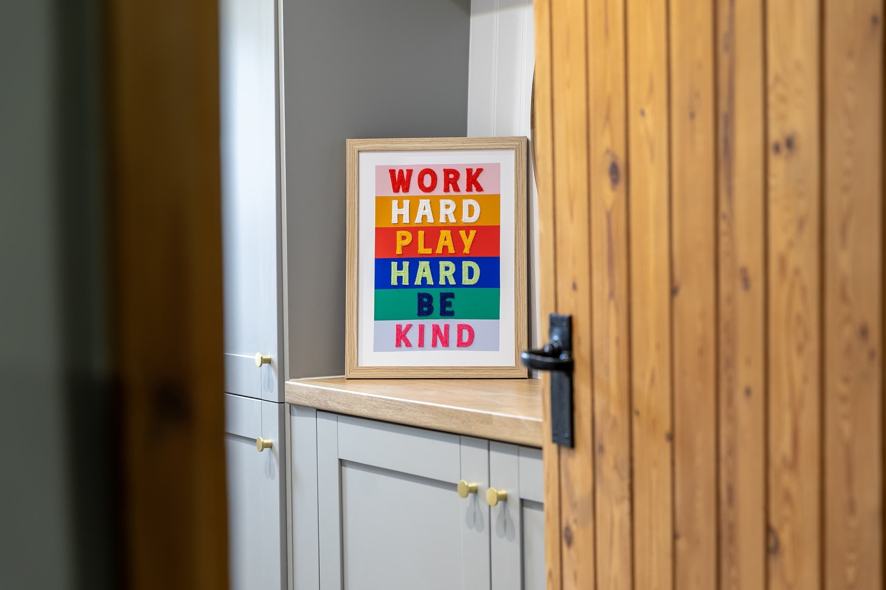A framed motivational quote on a wall in a room with wooden doors and white cabinets.