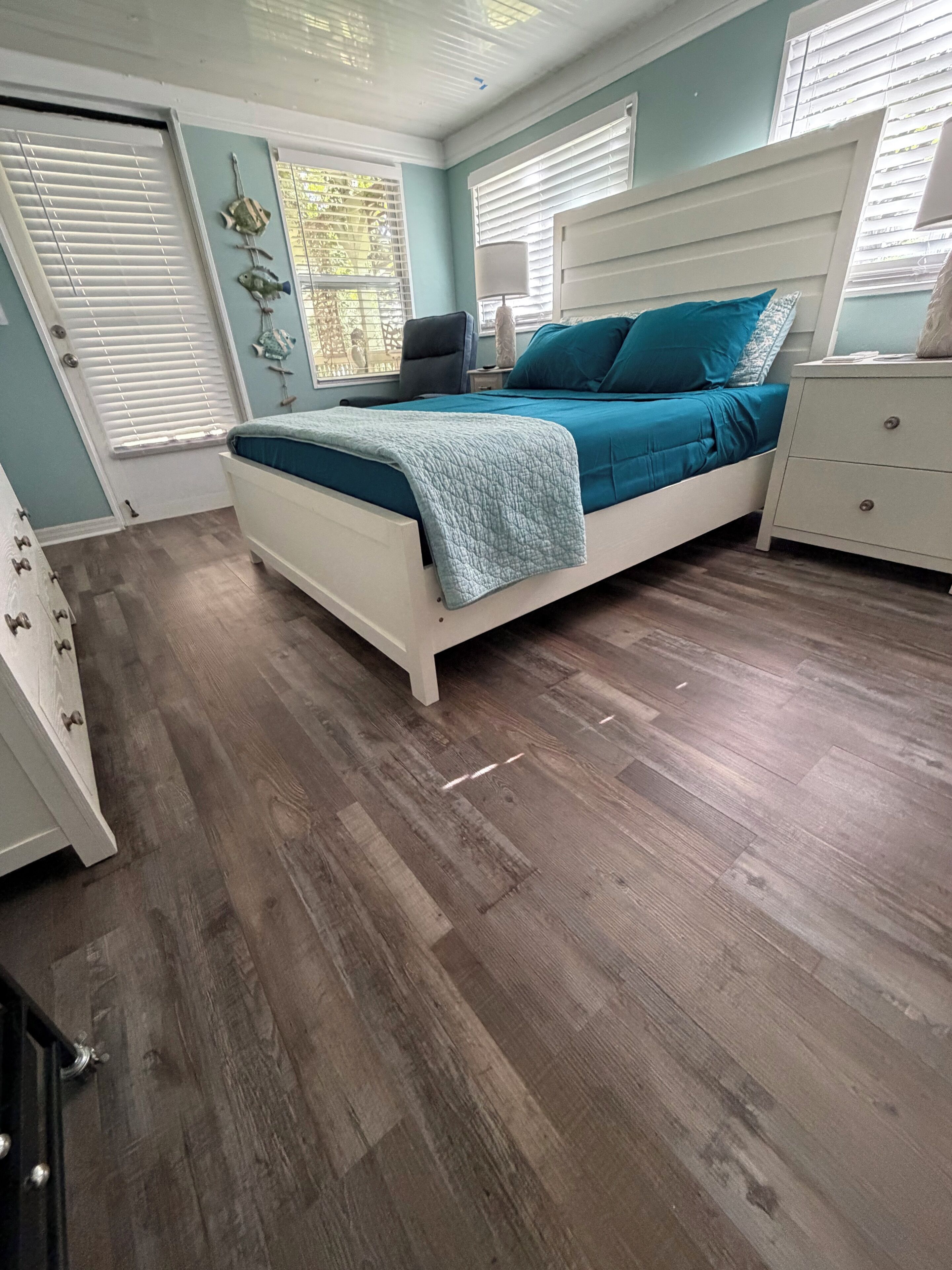 Une chambre à coucher comprenant un lit, une commode, une table de chevet et une fenêtre avec des stores.