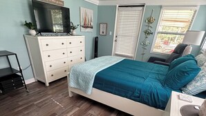 Un dormitorio con cama, cómoda, televisor y ventana con persianas.