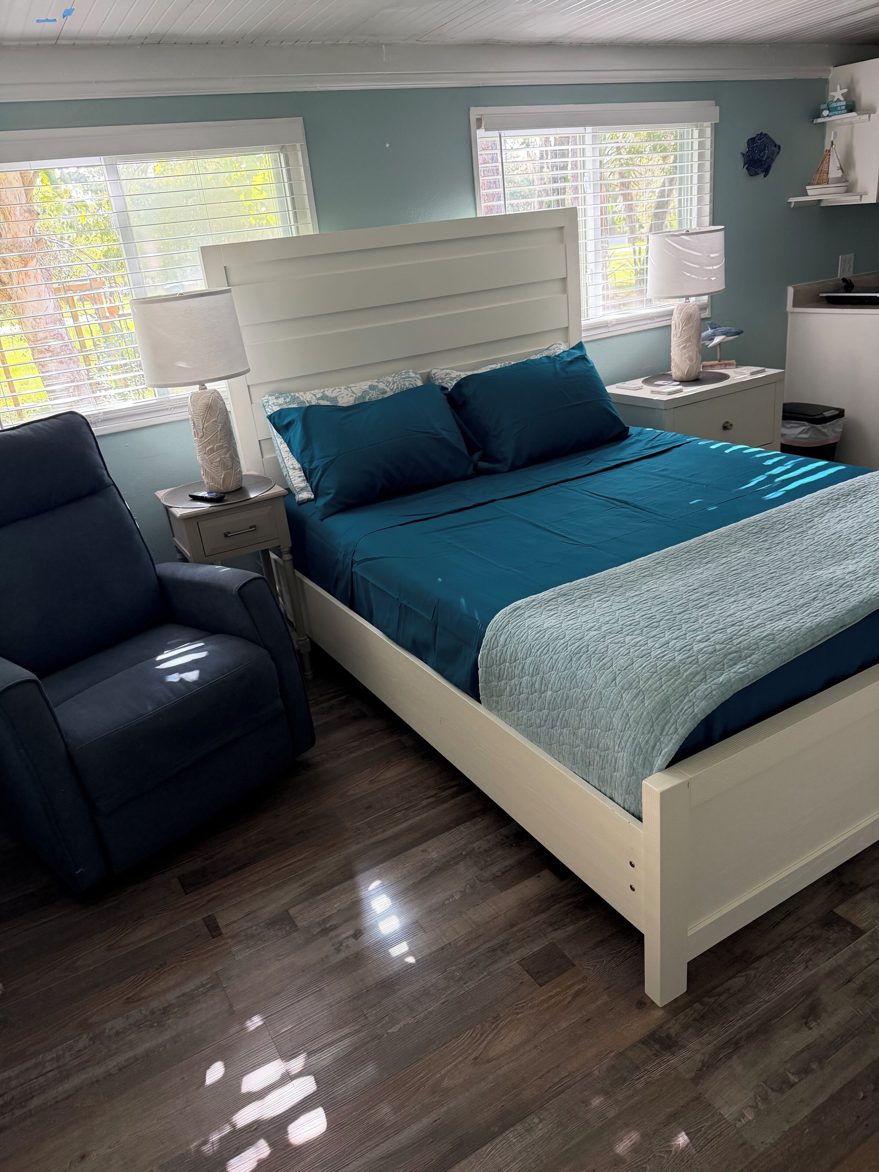A bedroom with a bed, a chair, a nightstand, a lamp, and a window with blinds.
