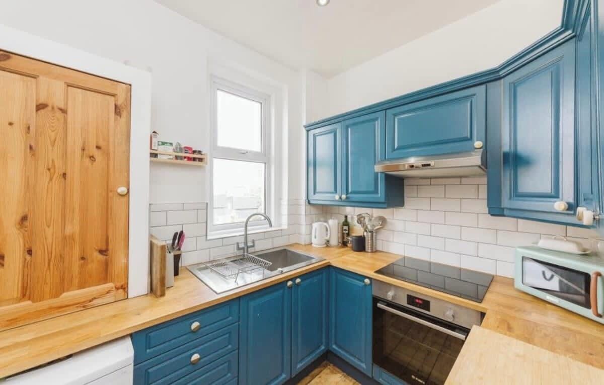 A kitchen with blue cabinets, a wooden countertop, a stainless steel sink, and a microwave.