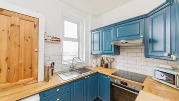 A kitchen with blue cabinets, a wooden countertop, a stainless steel sink, and a microwave.