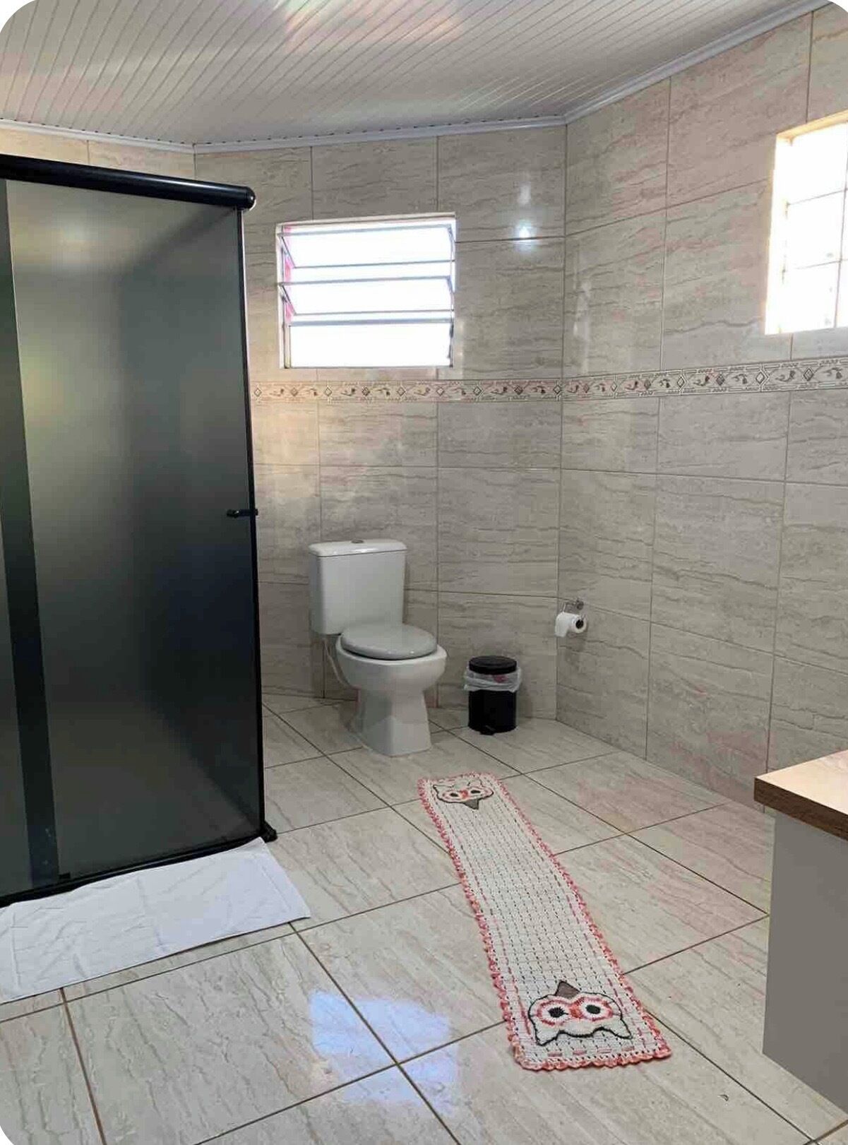 Un baño con inodoro, cubo de basura, ventana y puerta.