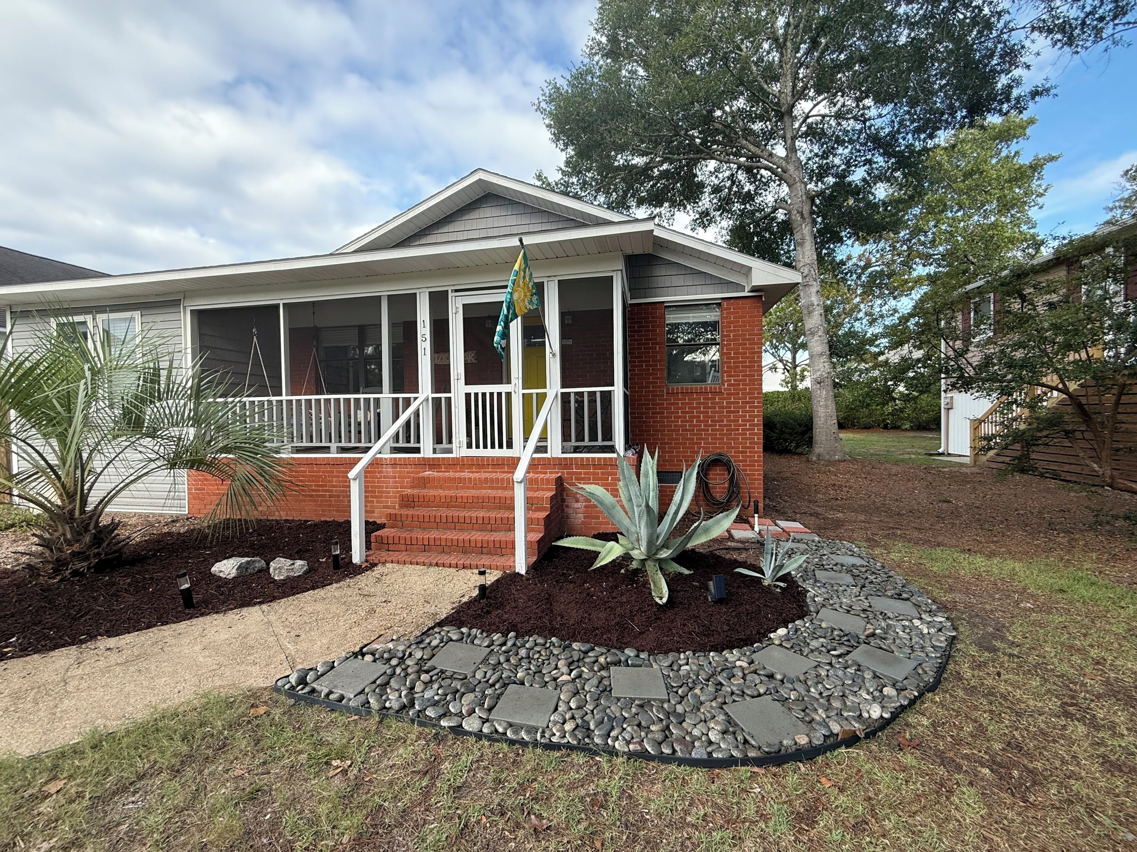A residential house with a brick facade, a covered porch, and a landscaped front yard with a stone pathway.