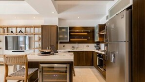 A modern kitchen with a central island, built-in appliances, and a dining area with a chair. - Urban by Pardela (Puerto Vallarta)