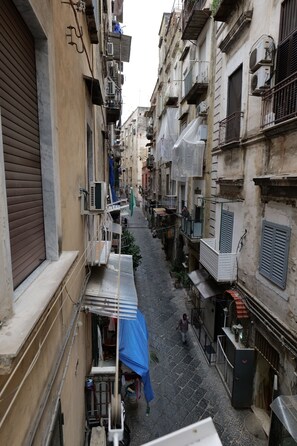 Une rue étroite en milieu urbain, bordée de bâtiments des deux côtés, avec des balcons et des unités de climatisation.