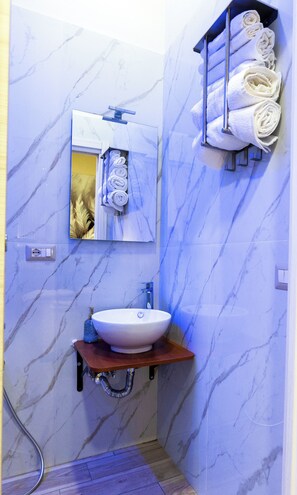 Une salle de bain avec un mur en marbre, un lavabo avec un plan de travail en bois, un porte-serviettes avec des serviettes pliées et un miroir.