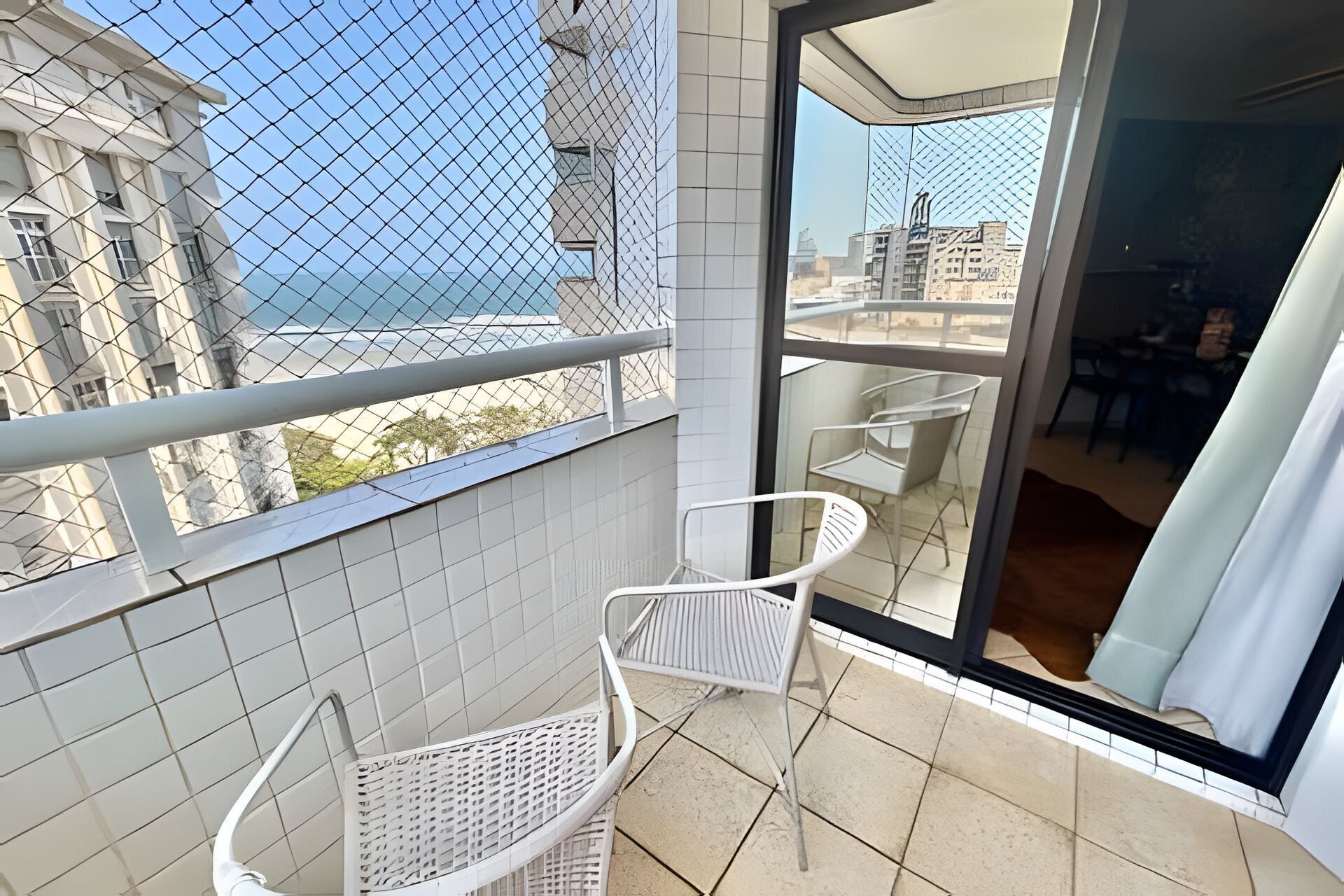 A balcony with white metal chairs and a glass door leading to an indoor area.