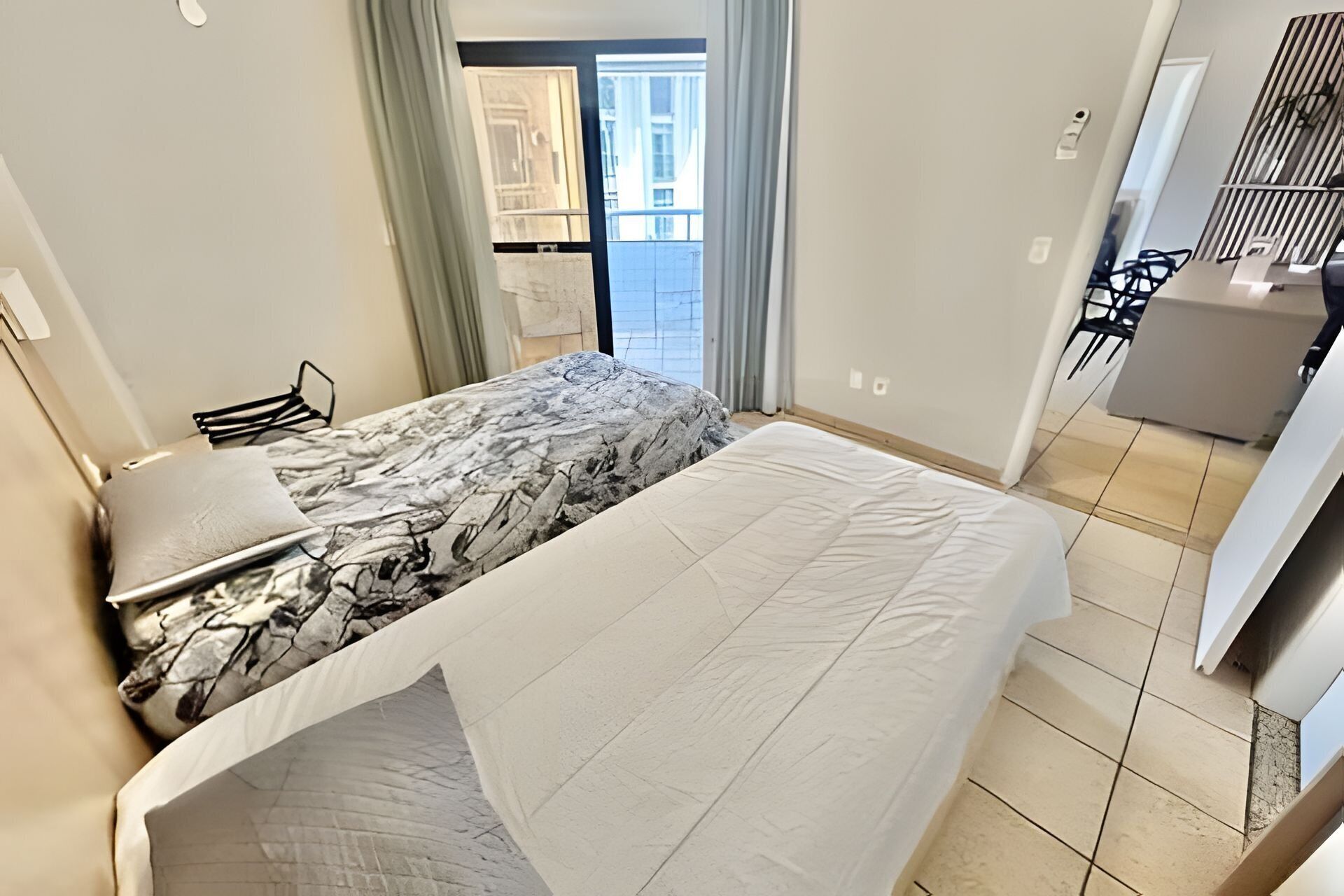A bedroom with a bed, a desk, and a chair. There is a window with curtains and a view of the outside.