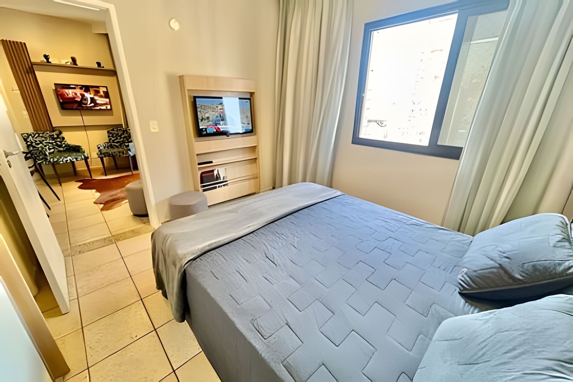 A hotel room with a bed, a TV, a seating area with chairs, and a window.