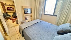 Hotellihuone, jossa on sänky, televisio, tuoleilla varustettu oleskelualue ja ikkuna.