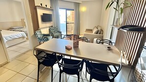 Un espacio habitable compacto con cama, una mesa de comedor con sillas, sofá, televisor montado en la pared y ventana con cortinas.