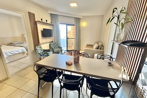 Un espacio habitable compacto con cama, una mesa de comedor con sillas, sofá, televisor montado en la pared y ventana con cortinas.
