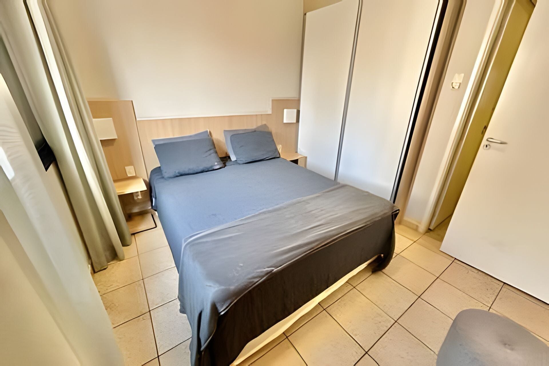 Quarto com cama, duas mesas de cabeceira, guarda-roupa e uma porta.