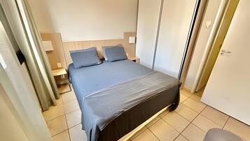 Quarto com cama, duas mesas de cabeceira, guarda-roupa e uma porta.
