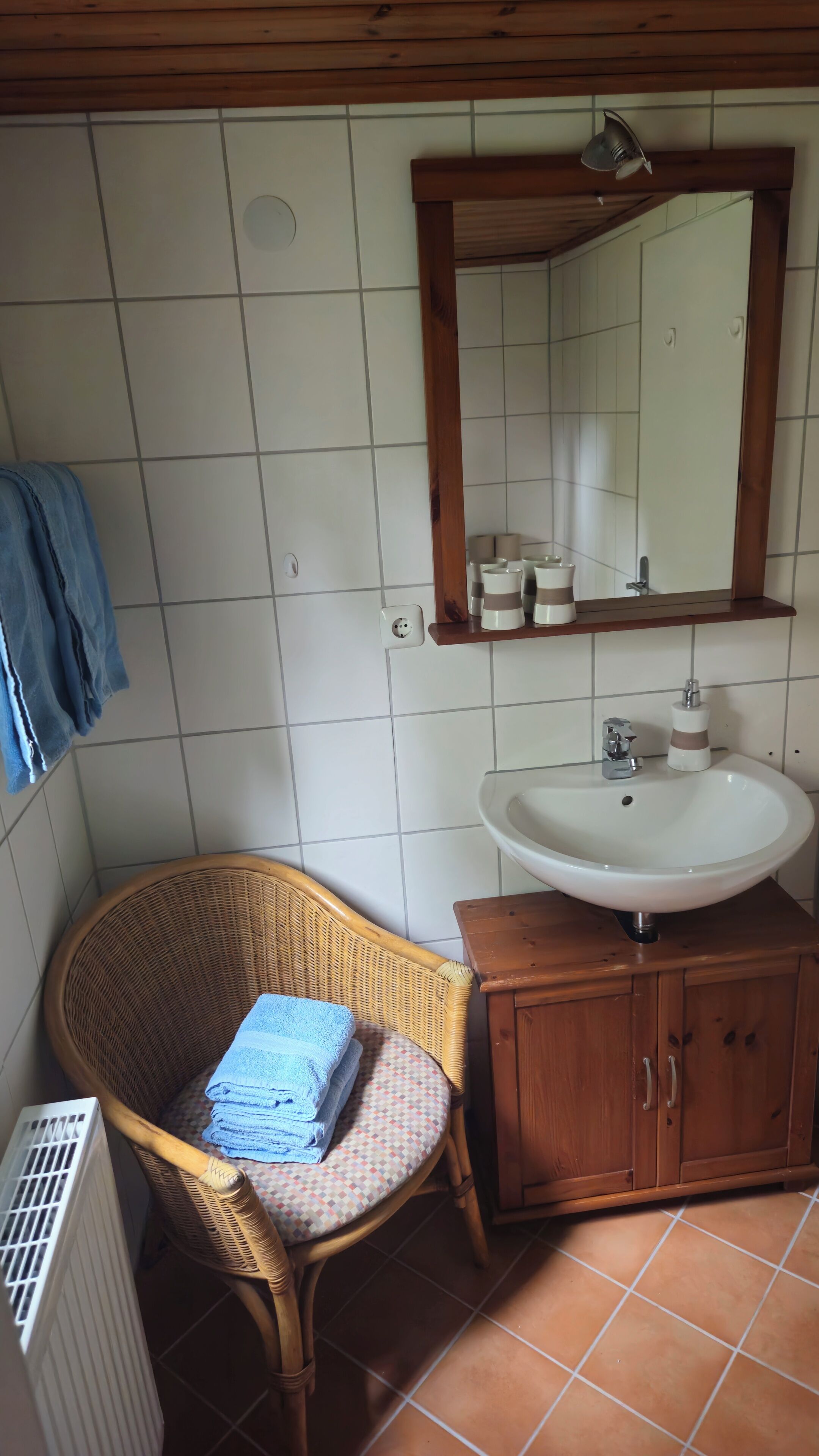 A bathroom with a white sink, wooden cabinet, wicker chair, and a towel.