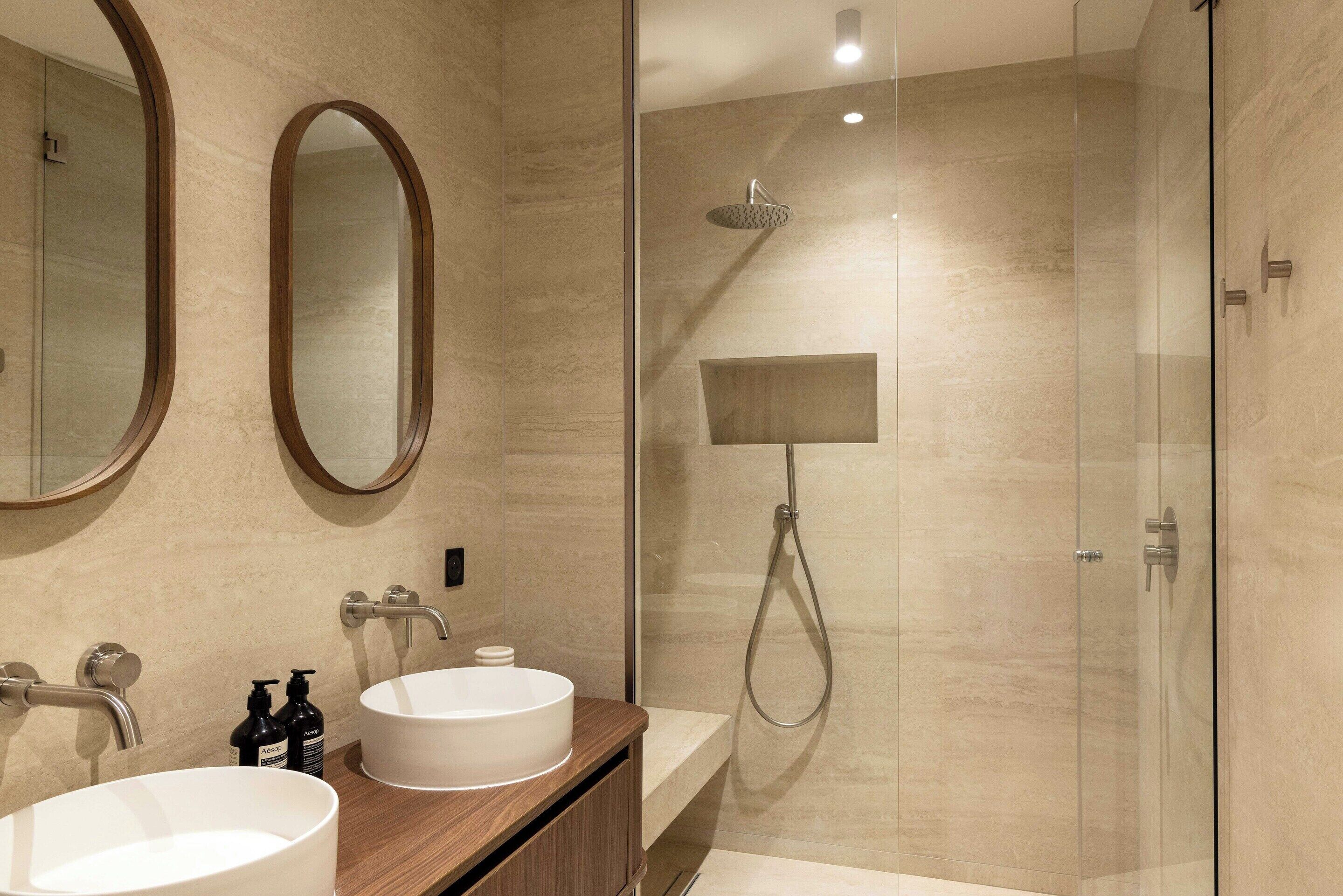 A modern bathroom with two sinks, a shower, and a mirror.