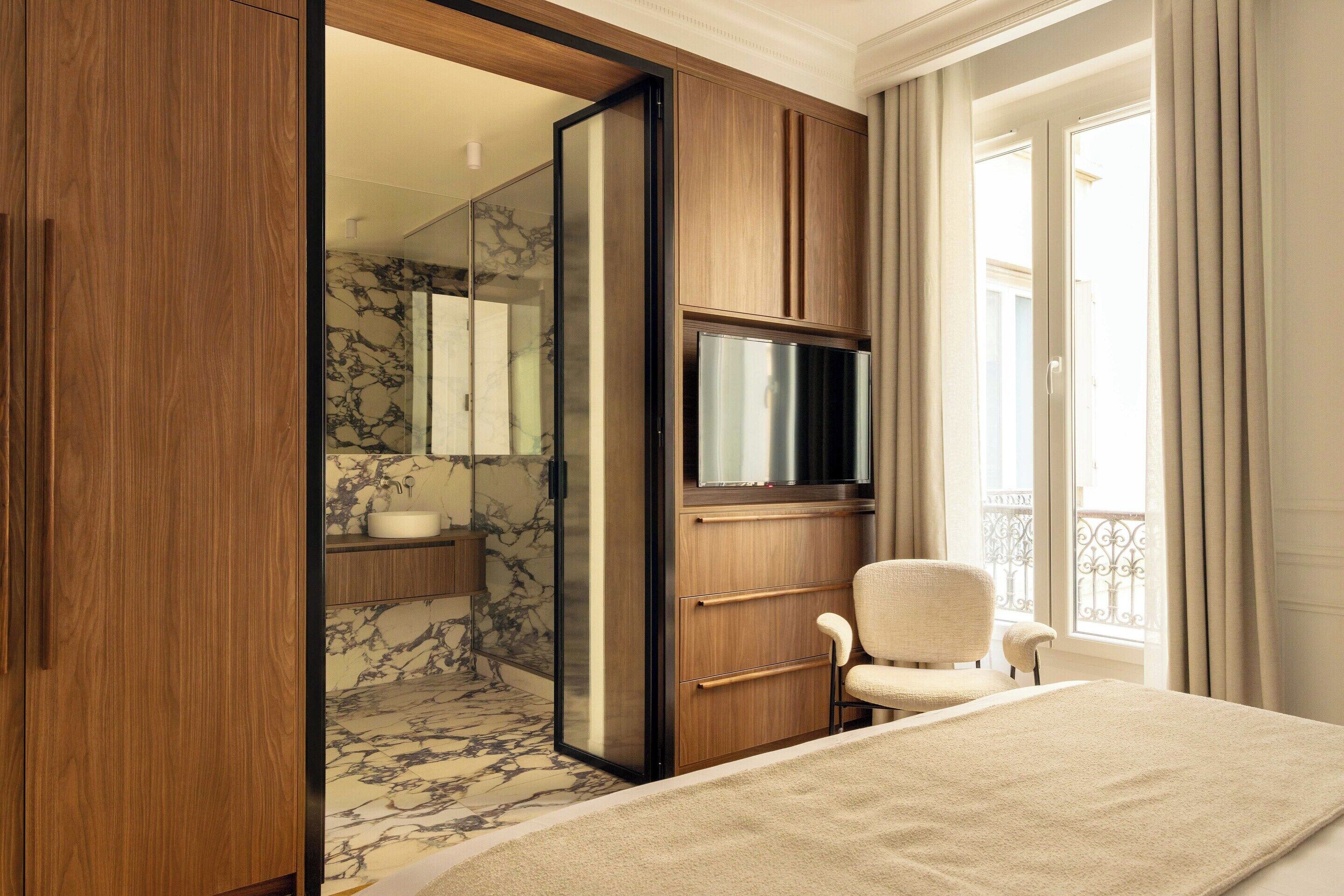 Une chambre à coucher comprenant un lit, une chaise, un téléviseur, une armoire et une salle de bain avec un sol en marbre.