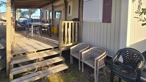Et overdækket udeområde med træterrasse, et bord med stole, og et lille lukket område med et vindue.