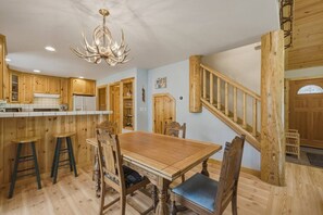 Een houten interieur met een eettafel, stoelen, een kroonluchter en een trap.