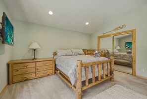 A bedroom with a wooden bed, a nightstand, a dresser, a mirror, and a painting on the wall. - The Rabbit Hole - Sauna. Soak. Repeat. (South Lake Tahoe)