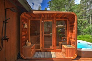 Een houten sauna met een glazen deur, een hottub en een klein terras.