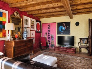 A living room with a wooden ceiling, a television, a sofa, a red wall, and various framed pictures. - Le Stanze degli Artisti by Case al Lago (Monzambano)