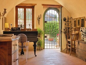 A room with a piano, a wooden cabinet, a chair, a table with books, and a large arched doorway leading outside. - Le Stanze degli Artisti by Case al Lago (Monzambano)