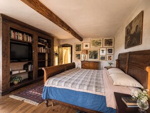 A bedroom with a wooden bed, a bookshelf, a television, and framed artwork on the wall. - Le Stanze degli Artisti by Case al Lago (Monzambano)