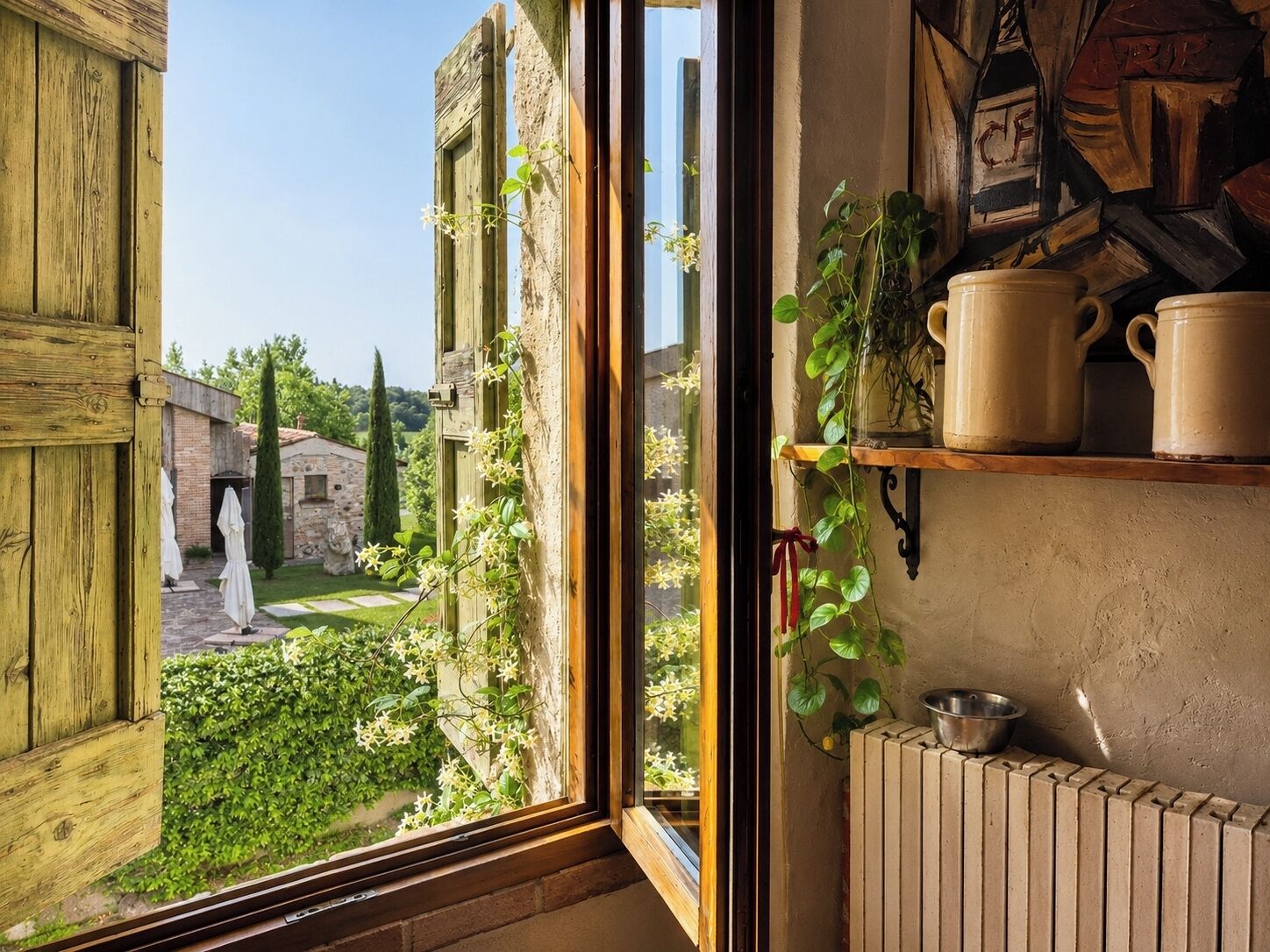 A rustic room with a large window, wooden shutters, a radiator, and a shelf with ceramic mugs.