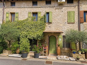 A stone building with green shutters, a green door, and potted plants. - Le Stanze degli Artisti by Case al Lago (Monzambano)