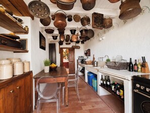 Eine Küche mit hängenden Töpfen, einem Holztisch, Stühlen, einer Arbeitsplatte mit Flaschen und einem Herd.
