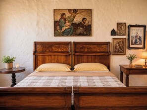 Ein Schlafzimmer mit einem hölzernen Bett, einem Nachttisch mit Lampe, einem Wandbild und einem kleinen Tisch mit Pflanze.