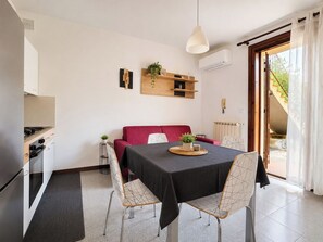 A modern dining area with a table set for two, a red sofa, and a kitchen in the background. - Iorek House by Case al Lago (Sirmione)