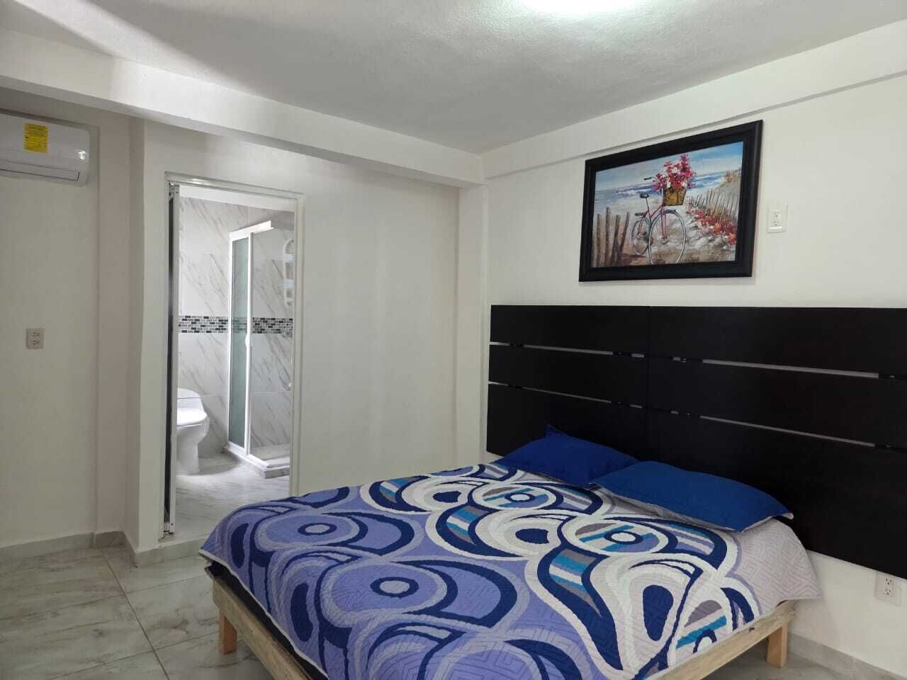 Une chambre à coucher avec un lit, une tête de lit, un espace douche et un tableau au mur.