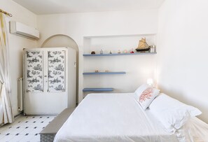 Un dormitorio con cama, armario, estante con adornos y radiador.