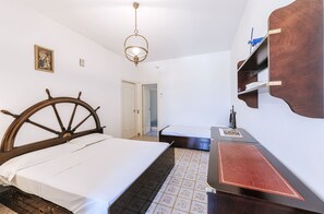 Ein Schlafzimmer mit einem Holzbett, einem kleinen Nachttisch, einem an der Wand befestigten Regal und einer Tür zu einem anderen Raum.