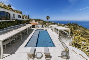 Una piscina con sillones de descanso, una pérgola y vistas al mar.
