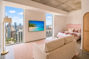 A modern hotel room with a large window, a bed with pink bedding, a beige sofa, and a cityscape view. - CD1608 - Downtown Loft with Pool, Gym and City Views in Miami (Miami Beach)