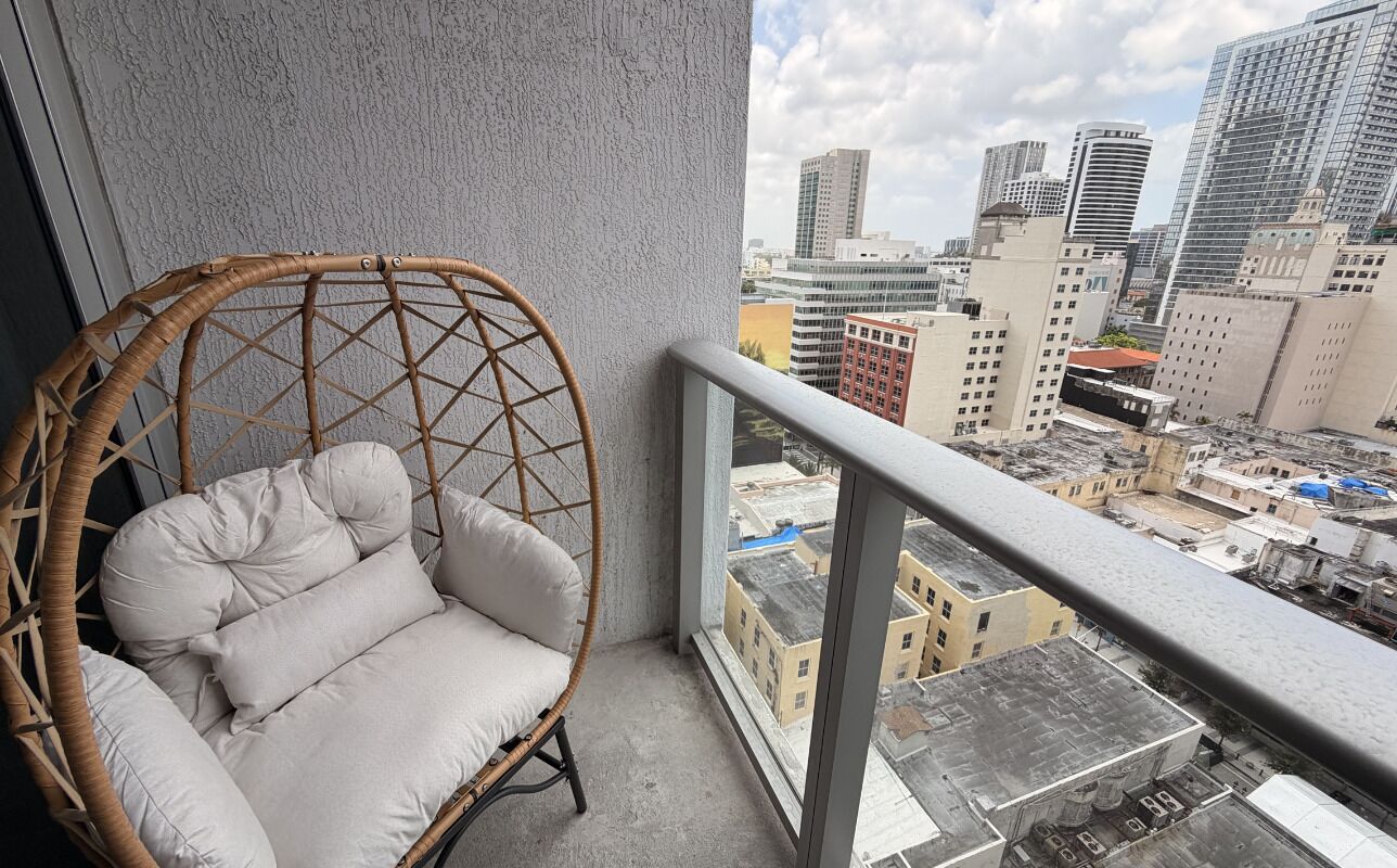 Une chaise en osier avec des coussins, sur un balcon offrant une vue sur la ville.