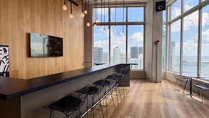 Eine moderne Bar mit einer langen Theke und mehreren Barhocker, große Fenster mit Blick auf die Stadt.