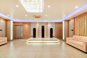 A spacious hotel lobby with a central seating area, recessed lighting, and a large chandelier.