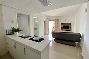 A modern kitchen with white cabinets, a central island, and a potted plant. - SHB Família à Beira-Mar Pé na Areia (Santos)