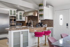 A modern kitchen with a central island, stainless steel appliances, and a white door. - Family Pool House Oasis (National City)