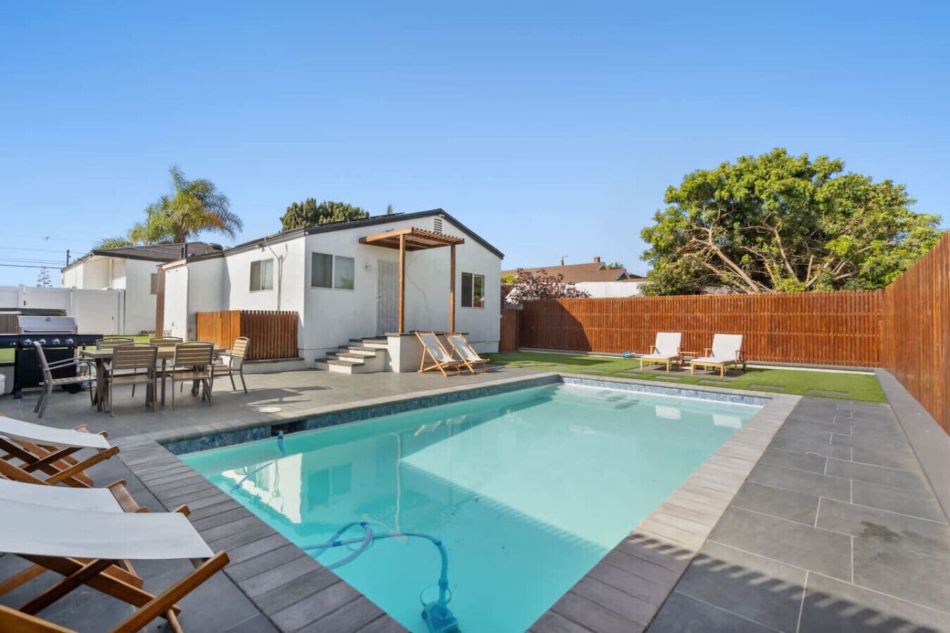 Un jardin avec une piscine, un espace barbecue et une petite terrasse avec des chaises.