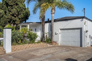 A residential property with a garage, a white exterior, and a landscaped front yard with palm trees and shrubs. - Family Pool House Oasis (National City)