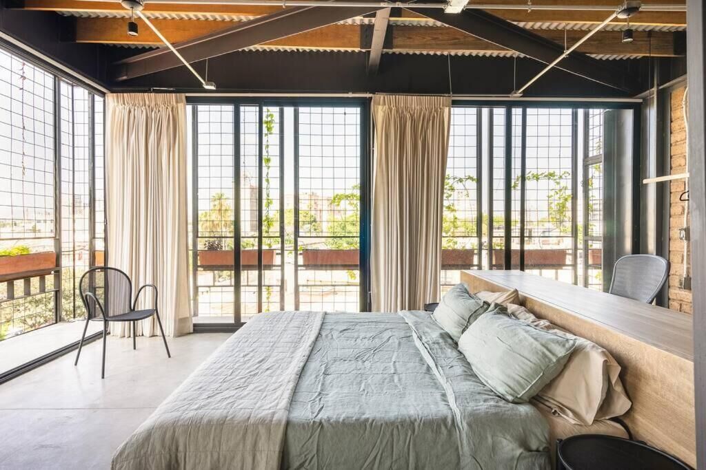 Un dormitorio con una cama grande, un escritorio y vistas al exterior a través de amplios ventanales.