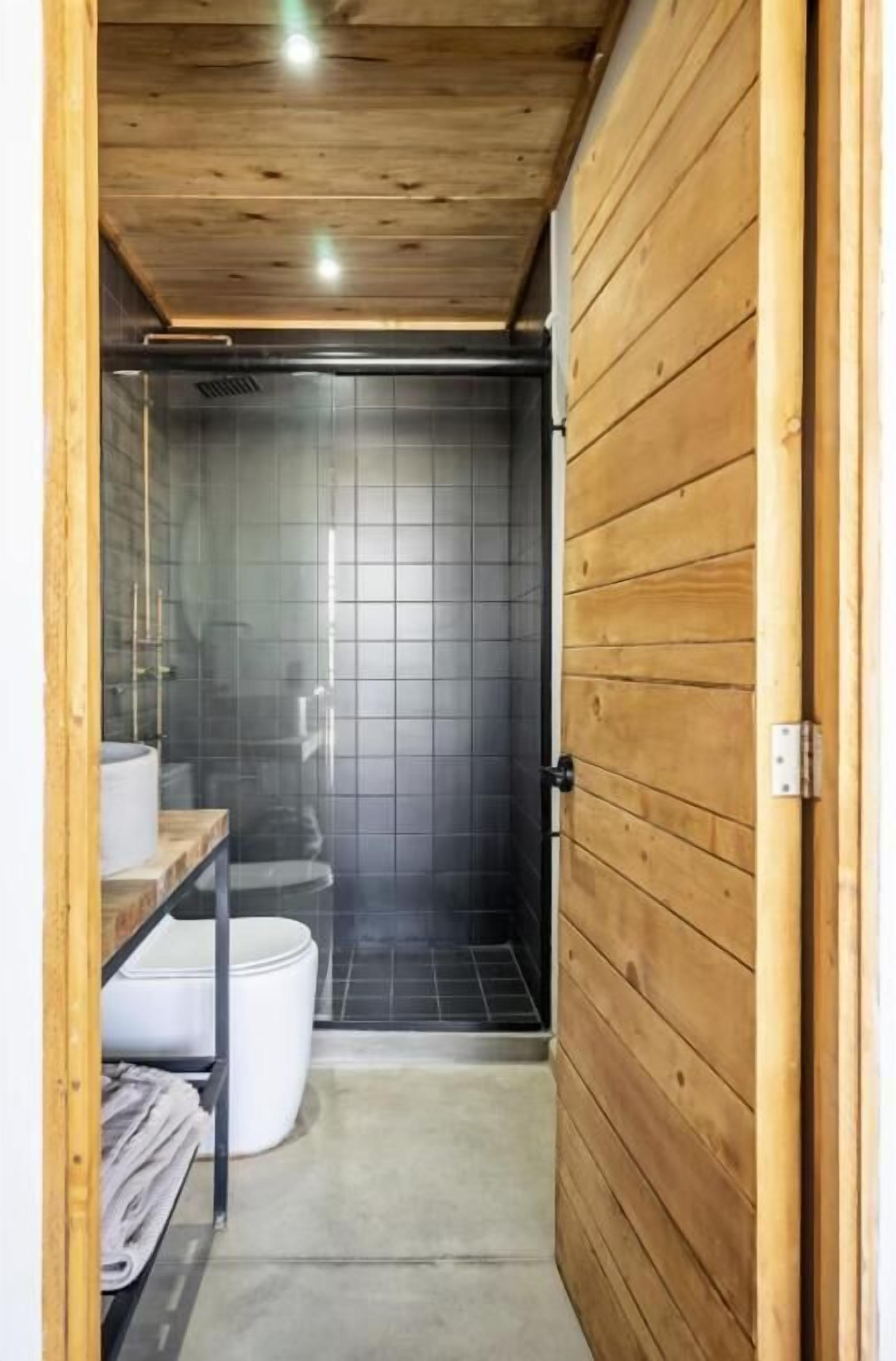 Un baño estrecho con puerta de madera, inodoro, lavabo y zona de ducha.