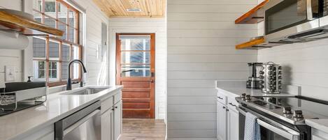 A modern kitchen with wooden ceiling, stainless steel appliances, and a view to the outside.